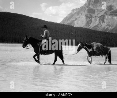 1940ER JAHRE COWBOY AUF PFERD KREUZUNG FLUß MIT 2. PFERD IM SCHLEPPTAU Stockfoto