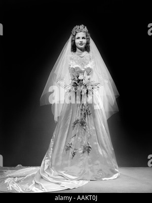 1940ER JAHRE FULL LENGTH PORTRAIT OF BRAUT IM HOCHZEITSKLEID BLICK IN DIE KAMERA Stockfoto