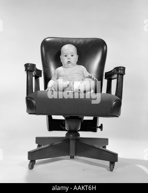 1960ER JAHREN BABYSITTER IM BÜROSESSEL BLICK IN DIE KAMERA Stockfoto