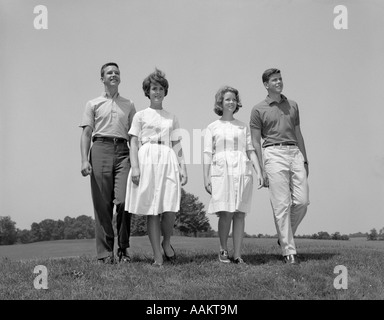 1960ER JAHRE ZWEI TEENAGER PAARE JUNGEN MÄDCHEN VOLLER LÄNGE SPAZIERGANG DURCH FELD IN RICHTUNG KAMERA Stockfoto