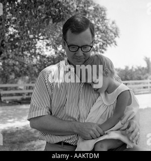 1970ER JAHREN VATER MIT TOCHTER DRAUßEN SITZEN AUF TRÖSTLICH IHR KNIE Stockfoto