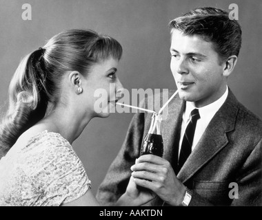 1950ER JAHRE TEENAGER-PAAR TEILEN EINE EINZELNE FLASCHE SODA MIT ZWEI STROHHALMEN Stockfoto