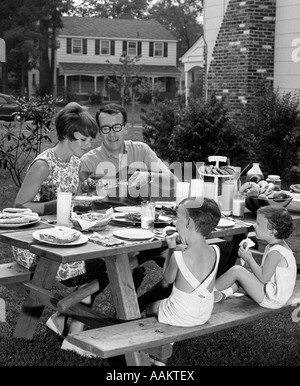 1960ER JAHREN S FAMILIE VON VIER AT-PICKNICK-TISCH IM HINTERHOF ESSEN Stockfoto