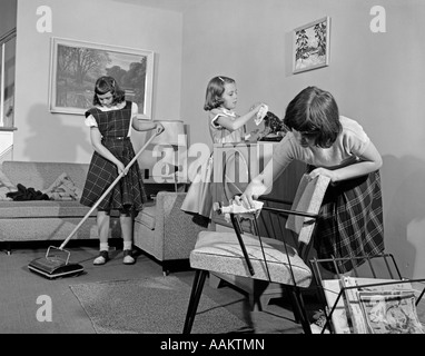 1950ER JAHREN DREI PRE-TEEN MÄDCHEN REINIGUNG LEBENDEN RAUM ABSTAUBEN STAUBSAUGEN Stockfoto