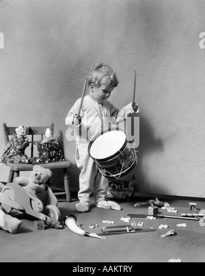 1930ER JAHRE JUNGE IM PYJAMA UMGEBEN VON SPIELZEUG ÜBER SPIELZEUG TROMMEL SCHLAGEN Stockfoto