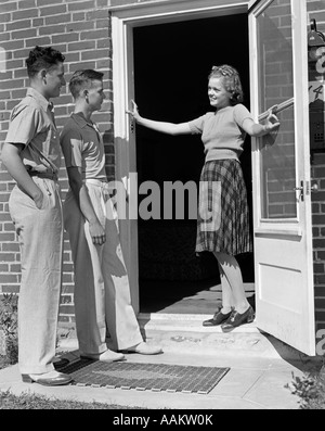 1930S 1940S TEEN MÄDCHEN LÄCHELN EINLADENDE ZWEI JUNGEN AN HAUSTÜR Stockfoto