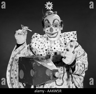 1960ER JAHREN CLOWN IN GEPUNKTETE OUTFIT UNTER BILD MIT ALTEN KAMERA MIT BIRDIE IN GEGENÜBERLIEGENDEN HAND Stockfoto