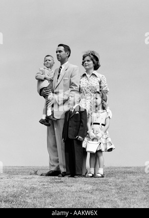 1950ER JAHREN FÜNFKÖPFIGE FAMILIE STEHEN IN EINER ENGEN GRUPPE, DIE SIE ALLE, DER VATER ANGEZOGEN HÄLT DER KLEINSTE JUNGE Stockfoto