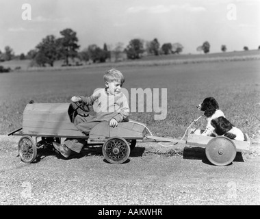 1930S 1940S JUNGE IN HOLZSPIELZEUG AUTO ZIEHEN HUND HINTER WAGEN Stockfoto