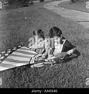 1940ER JAHRE GRASS MÄDCHEN UND JUNGE SITZT IM RASEN HOLDING AMERIKANISCHE FLAGGE STIL KITE Stockfoto