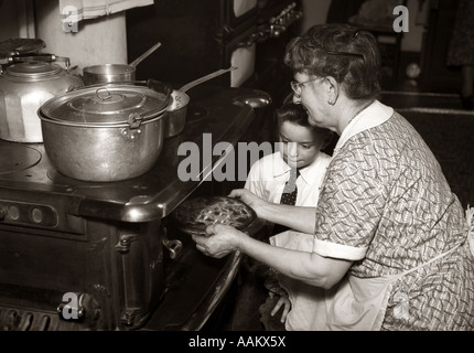 1930S 1940S BOY BEOBACHTEN GROßMUTTER NEHMEN PIE AUS GUSSEISEN HOLZOFEN OFEN OFEN Stockfoto