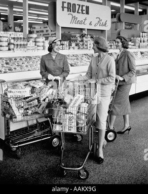 1950ER JAHREN DREI FRAUEN DRÄNGEN SHOPPING CARTS TREFFEN REDEN IN TIEFKÜHLKOST GANG DES SUPERMARKTES Stockfoto