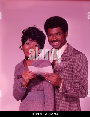 1970ER JAHREN AFRIKANISCHE AMERIKANISCHE PAAR LÄCHELND HOLDING ÜBERPRÜFEN Stockfoto