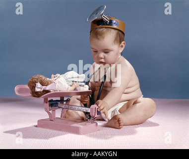 BABY TRAGEN ARZT SPIEGEL STIRNBAND MIT EINEM GEWICHT VON PUPPE AUF BALANCE SKALA Stockfoto