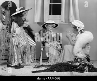 1950ER JAHRE JUNGE & ZWEI MÄDCHEN TRAGEN ERWACHSENE KLEIDUNG, LÄCHELN UND HALTEN GLÄSER MILCH DRESS UP SPIELEN Stockfoto