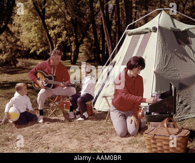 ELTERN MIT SOHN UND TOCHTER AUßERHALB ZELT SPIELEN GITARRE UND KOCHEN AM GRILL VIER MANN FRAU JUNGE MÄDCHEN URLAUB DER 1960ER JAHRE Stockfoto