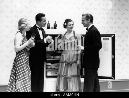 1930S 1940S GEKLEIDET ZWEI PAARE FÖRMLICH VOR KÜHLSCHRANK MIT TÜREN OFFEN TRINKEN BIER Stockfoto