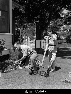 1930S 1940S VATER & SOHN TUN HOF ARBEITEN JUNGE STÜTZTE SICH AUF PUSH-RASENMÄHER & MANN KNIENDE ARBEITEN IM BLUMENBEET Stockfoto