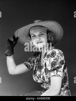 1930S 1940S PORTRAIT FRAU IM STROHHUT GEBLÜMTEN KLEID HAND MIT HUT TRAGEN HANDSCHUHE, BLICK IN DIE KAMERA Stockfoto