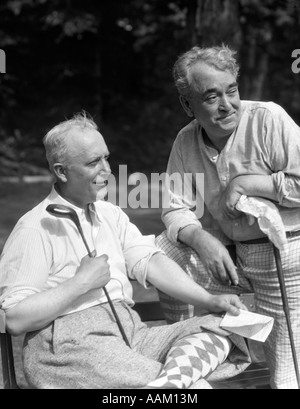 1930ER JAHREN GOLF 2 ÄLTERE MÄNNER TRAGEN KLEIDUNG SCHLÜPFER ARGYLE GOLFSOCKEN HÄLT LÄCHELND, CLUBS UND NOTENBLATT Stockfoto