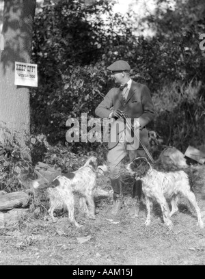 1930ER JAHRE MANN MIT ZWEI HUNDE HALTEN SIE SCHROTFLINTE LESUNG SCHILD AM BAUM SAGEN KEINE JAGD KEIN HAUSFRIEDENSBRUCH WAFFEN ODER HUNDE FERNZUHALTEN Stockfoto