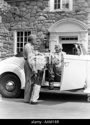 1940ER JAHRE SENIOR IM RUHESTAND PAAR LADEN GOLFCLUBS IN WEIßEN CABRIO VORNE STEINHAUS Stockfoto