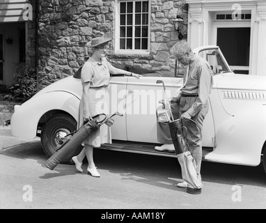 1930S 1940S ÄLTERES PAAR SETZEN GOLFCLUBS IM CABRIO VON HAUS AUS STEIN Stockfoto