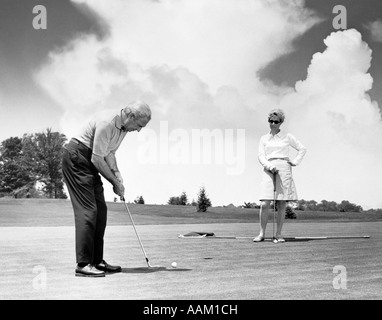 1960ER JAHRE ÄLTERES EHEPAAR AUF GOLF GRÜNER MANN SETZEN Stockfoto