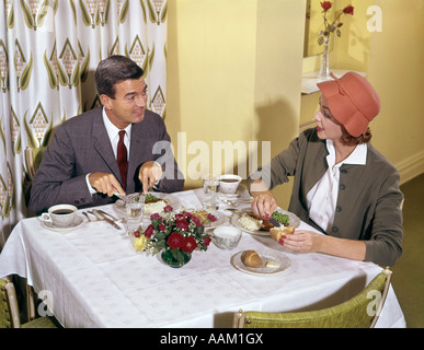 1950S 1960S PAAR MANN FRAU ESSEN IM RESTAURANT TABLE PRINT VORHÄNGE HINTER MANN FRAU TRAGEN ORANGE HUT ESSEN Stockfoto