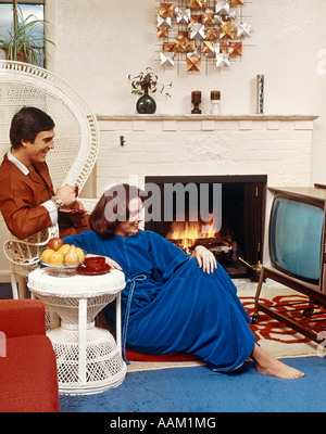 1970ER JAHREN PAAR IM WOHNZIMMER SITZEN VOR FERNSEHER UND NEBEN EINEM FEUER Stockfoto