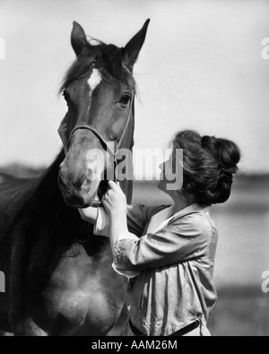 1900S 1910S JUNGE FRAU MIT HOCHGEZOGENER HAAR HOLDING PFERD DURCH HALTER Stockfoto