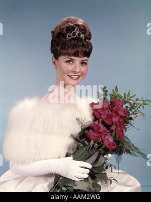 1960ER JAHREN STAHLEN JUNGE FRAU TRÄGT KRONE WEIßEN FELL HANDSCHUHE HALTEN STRAUß ROTER ROSEN Stockfoto