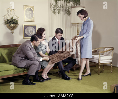 FRAU ZEIGT PELZMANTEL, ZWEI MÄNNER UND EINE FRAU IM WOHNZIMMER INDOOR LIFESTYLE GESCHENK Stockfoto
