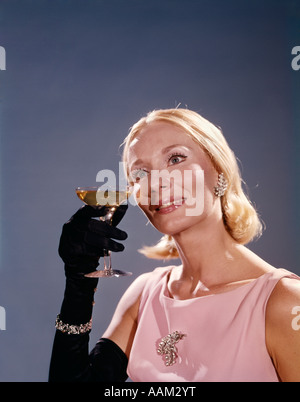 1960ER JAHREN LÄCHELNDEN BLONDEN FRAU ROSA KLEID SCHWARZE HANDSCHUHE SCHMUCK HOLDING GLAS CHAMPAGNER TOAST TOASTEN Stockfoto