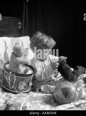 1930ER JAHRE JUNGE IM BETT MIT EINEM BALL & TEDDYBÄR SITZEND AUF EINEM SPIELZEUG TROMMEL TRAGEN SCHLAFANZUG SPIELEN Stockfoto