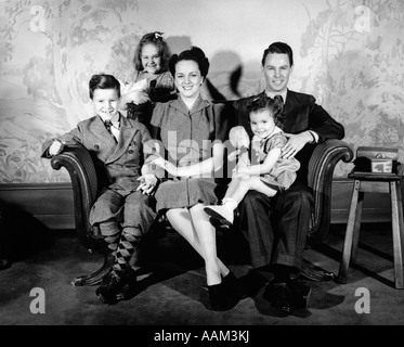 1940ER JAHRE FAMILIE VON 5 PORTRÄT SITZEN AUF DER COUCH VOR KAMERA LÄCHELNDE MUTTER VATER ZWEI MÄDCHEN EINE JUNGE WALLPAPER IM HINTERGRUND DRUCKEN Stockfoto