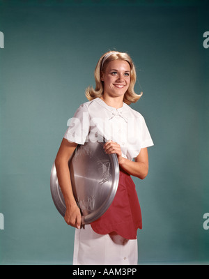 1960ER JAHREN FRAU IM WEIßEN KLEID ROT SCHÜRZE MIT SILBERNEN TABLETT KELLNERIN SERVER Stockfoto