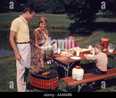 1960ER JAHRE FAMILIE VATER MUTTER ZWEI SÖHNE TOCHTER GENIEßEN OUTDOOR-BAR-B-CUE Stockfoto