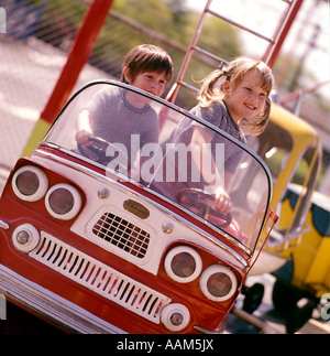 1970ER JAHREN ZWEI KINDER KINDER JUNGEN MÄDCHEN SPIELEN SPIELZEUG BUS AUTO FEUER LKW FIRE ENGINE VERGNÜGUNGSPARK FAHREN FAHREN Stockfoto