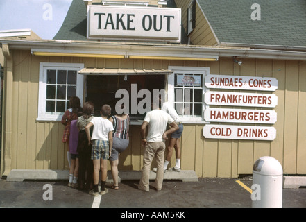 1970ER JAHRE GRUPPE VON MENSCHEN BEI HERAUSNEHMEN FASTFOOD THEKE FENSTER EISBECHER KEGEL KALTE GETRÄNKE HAMBURGER WÜRSTCHEN IM FREIEN Stockfoto