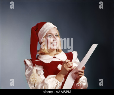 1960ER JAHRE JUNGE FRAU IN SANTA HELFER HUT UND KOSTÜM HOLDING PEN UND LISTE SYMBOLISCHE PORTRAIT Stockfoto