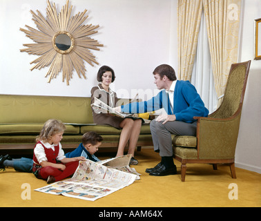 1970ER JAHREN MUTTER UND VATER LESUNG SONNTAGSZEITUNG MIT SOHN UND TOCHTER IM WOHNZIMMER SUNBURST SPIEGEL MANN FRAU JUNGE MÄDCHEN Stockfoto