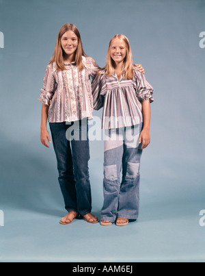 ZWEI MÄDCHEN IM TEENAGERALTER IN 1970 1970S KLEIDUNG STEHEND ARME UMEINANDER LÄCHELND Stockfoto