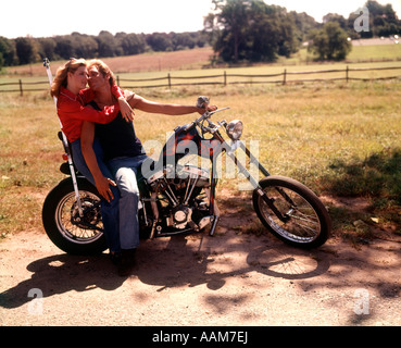 1970 1970S MANN PAAR FRAU UMARMT ROMANTISCHE SITZEN AUF CHOPPER-MOTORRAD-BIKE-MOTORRAD-MOTORRÄDER-FAHRRÄDER Stockfoto