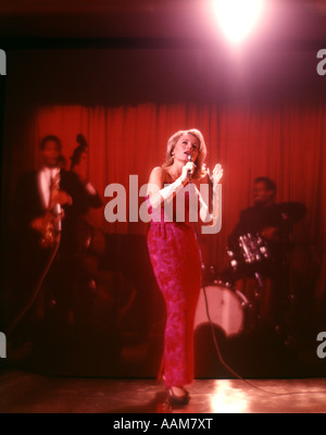 1970 1970S BLONDE FRAU SÄNGER LANGEN ROSA ROTEN KLEID WEIßE HANDSCHUHE AUF DER BÜHNE BACKUP MUSIKER SÄNGER SÄNGER SINGEN Stockfoto