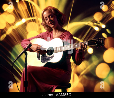 1970 1970S SÄNGERIN FRAU SINGEN SPIELEN GITARRE SITZEN HOCKER MIKROFON AKUSTISCHE FOLK-SÄNGERIN ROSA KLEID Stockfoto