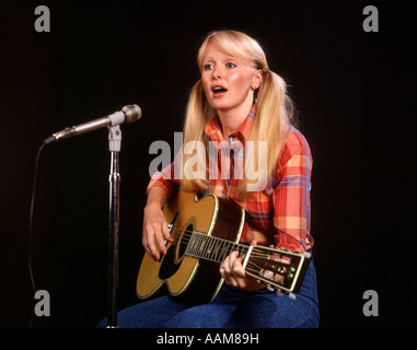 1970 1970S BLOND BLONDE JUNGE FRAU ZÖPFEN KARIERTES HEMD JEANS SPIELEN GITARRE GESANG MIKROFON FOLK-SÄNGERIN SÄNGER Stockfoto