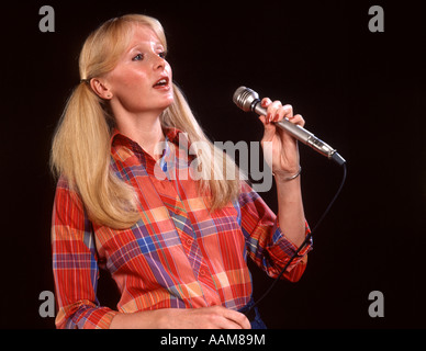 1970 1970S BLOND BLONDE FRAU ZÖPFEN LANGHAAR MIKROFON KARIERTES HEMD SÄNGER SÄNGERIN GESANG VOLKSMUSIK ENTERTAINER Stockfoto