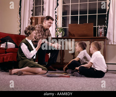 1960ER JAHREN VERSAMMELTE PLATTENSPIELER ANHÖREN VON MUSIK INDOOR WOHNZIMMER MANN-FRAU JUNGE FAMILIE MIT ZWEI SÖHNEN Stockfoto