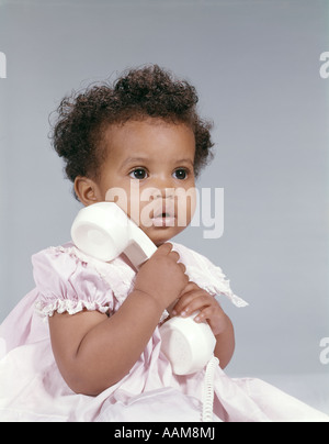 AFRICAN-AMERICAN BABYMÄDCHEN IM ROSA KLEID HOLDING TELEFON Stockfoto